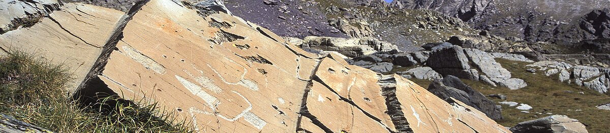 Veduta ravvicinata di alcune incisioni rupestri della Vallée des Merveilles, con figure simboliche tracciate su grandi lastre di pietra immerse in un paesaggio alpino roccioso. Archivio APAM. Fine descrizione dell’immagine.
